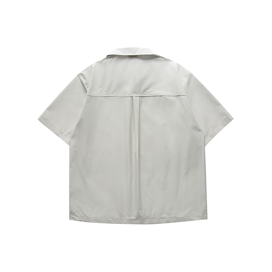 Back view of pale gray-green short-sleeve shirt with yoke seam and center pleat, flat lay