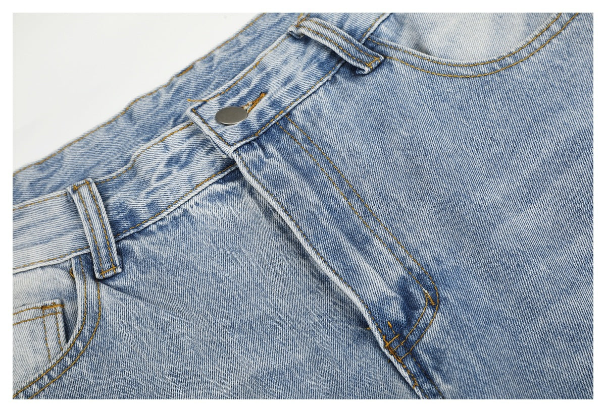 Close-up of light blue washed jeans showing the metal waist button, belt loop, fly seam, and contrast stitching.