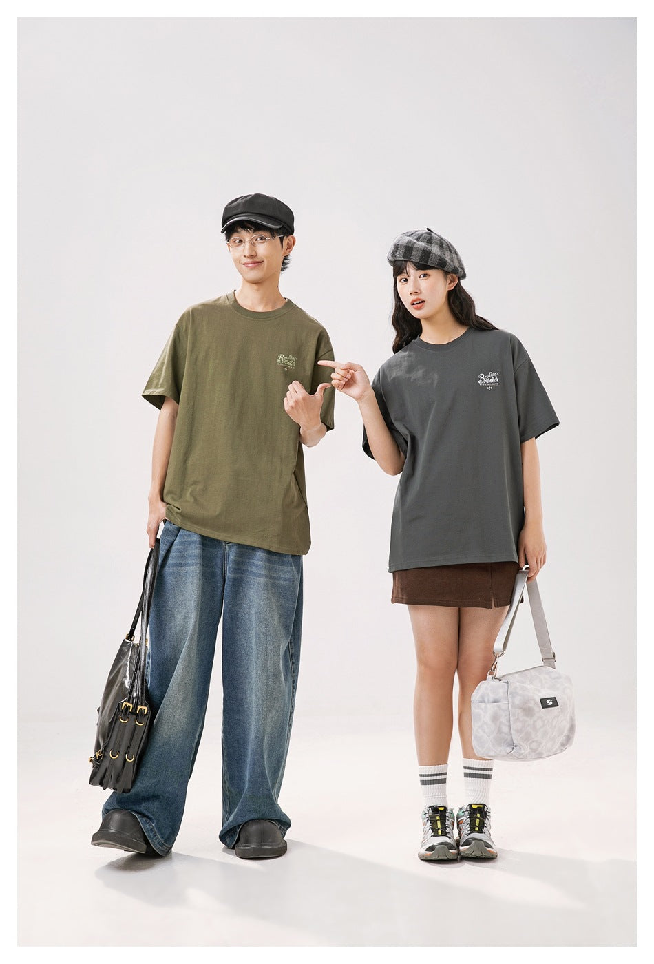 Two models show olive and charcoal oversized T-shirts with small chest prints from the front.