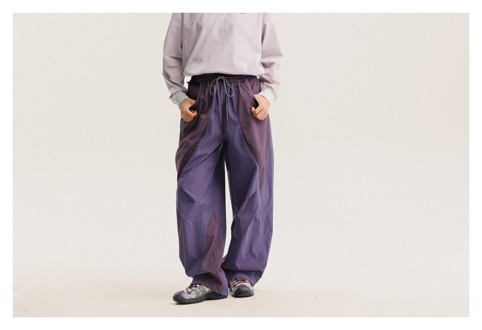 Front view of a model wearing loose purple paneled pants with a drawstring waist and side pockets.