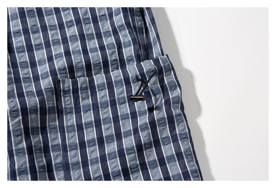 Close-up of a plaid pant pocket with a black drawcord toggle and blue, gray, and white stripes.