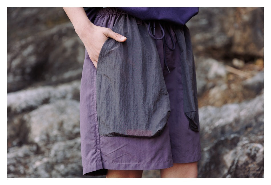 Close-up of purple shorts showing the large charcoal front pocket, elastic waist and drawcord.