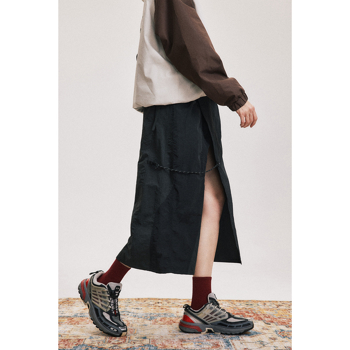 Side view of a model wearing a black mid-calf skirt with a high side slit and a cord detail.