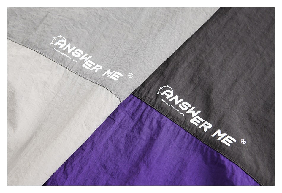 Close-up of the white ANSWER ME logo printed across gray and charcoal-purple jacket panels.