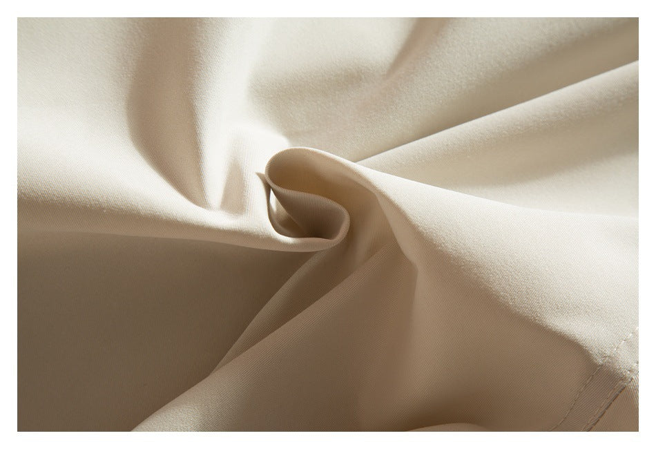 Close-up of light beige trouser fabric arranged in soft folds, showing its smooth surface and seam.