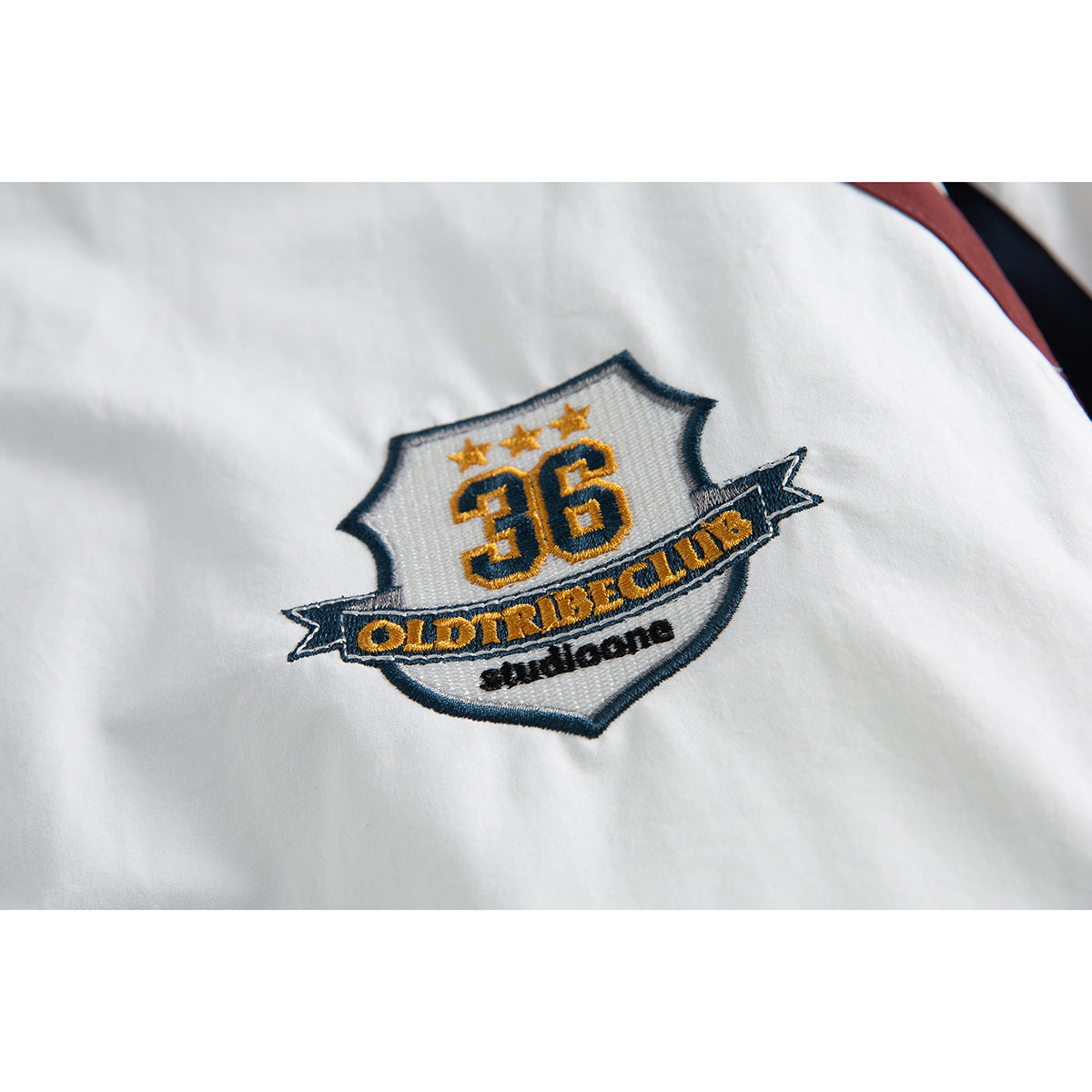 Close-up of a gold, navy and white embroidered shield patch with the number 36 on a white jacket.