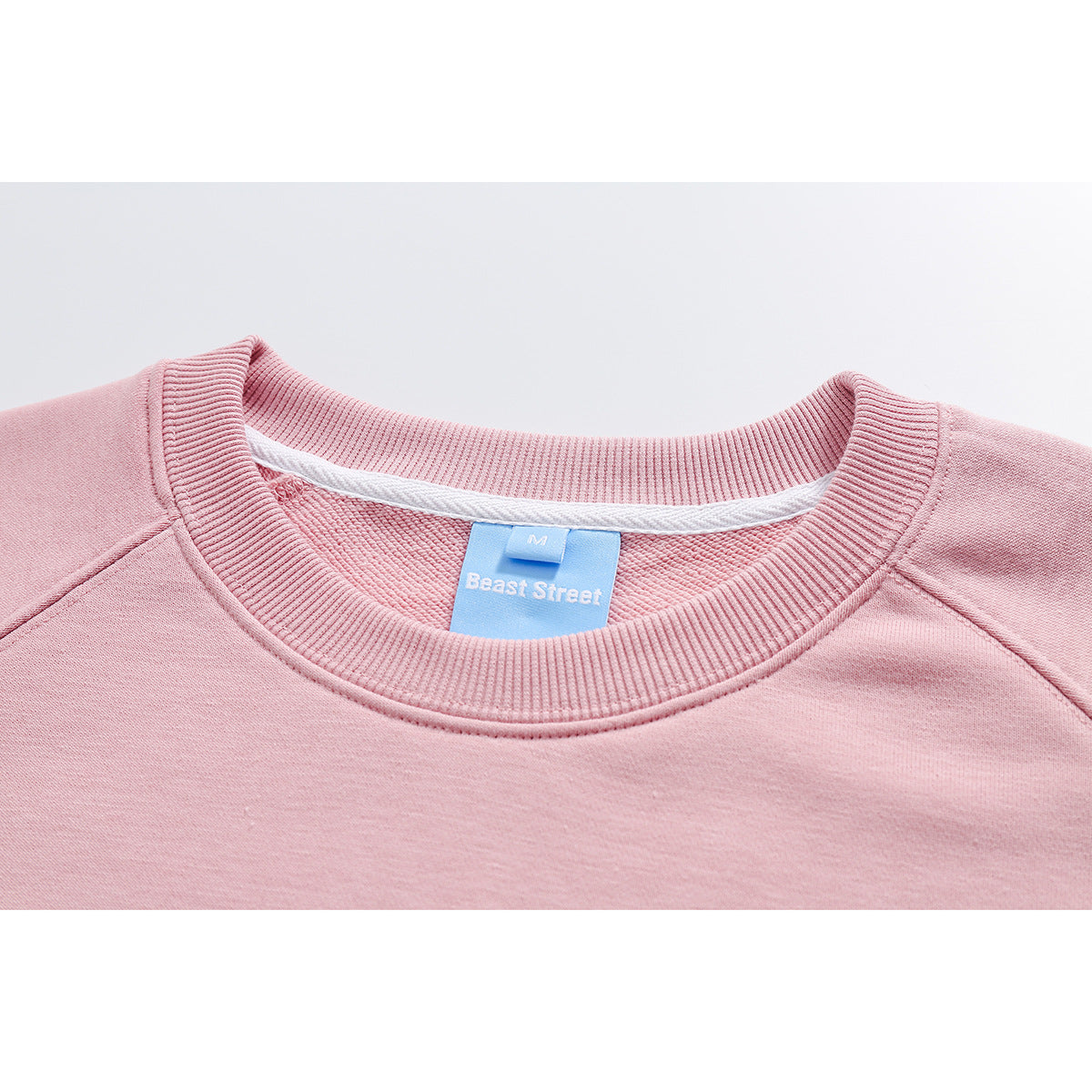 Close-up of a pale pink sweatshirt's ribbed crew neckline and blue Beast Street label.