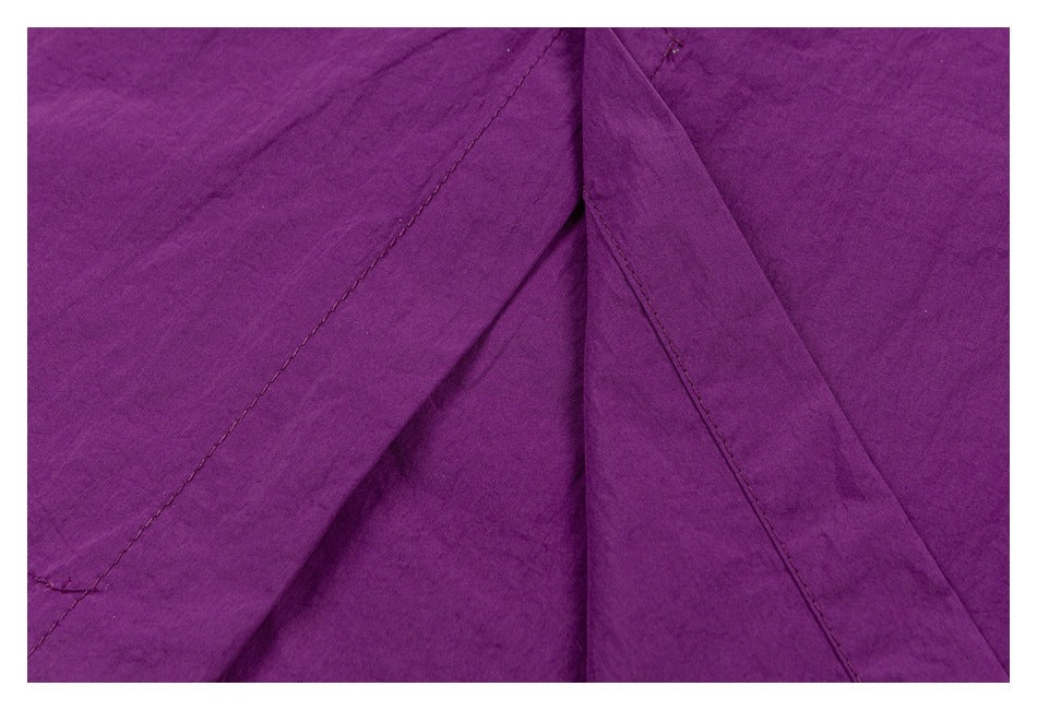 Close-up of purple garment fabric with diagonal stitched seams and overlapping panels.