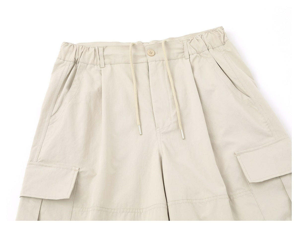 Front view of light beige cargo trousers with a gathered drawstring waist, button, slant pockets and flap cargo pockets.