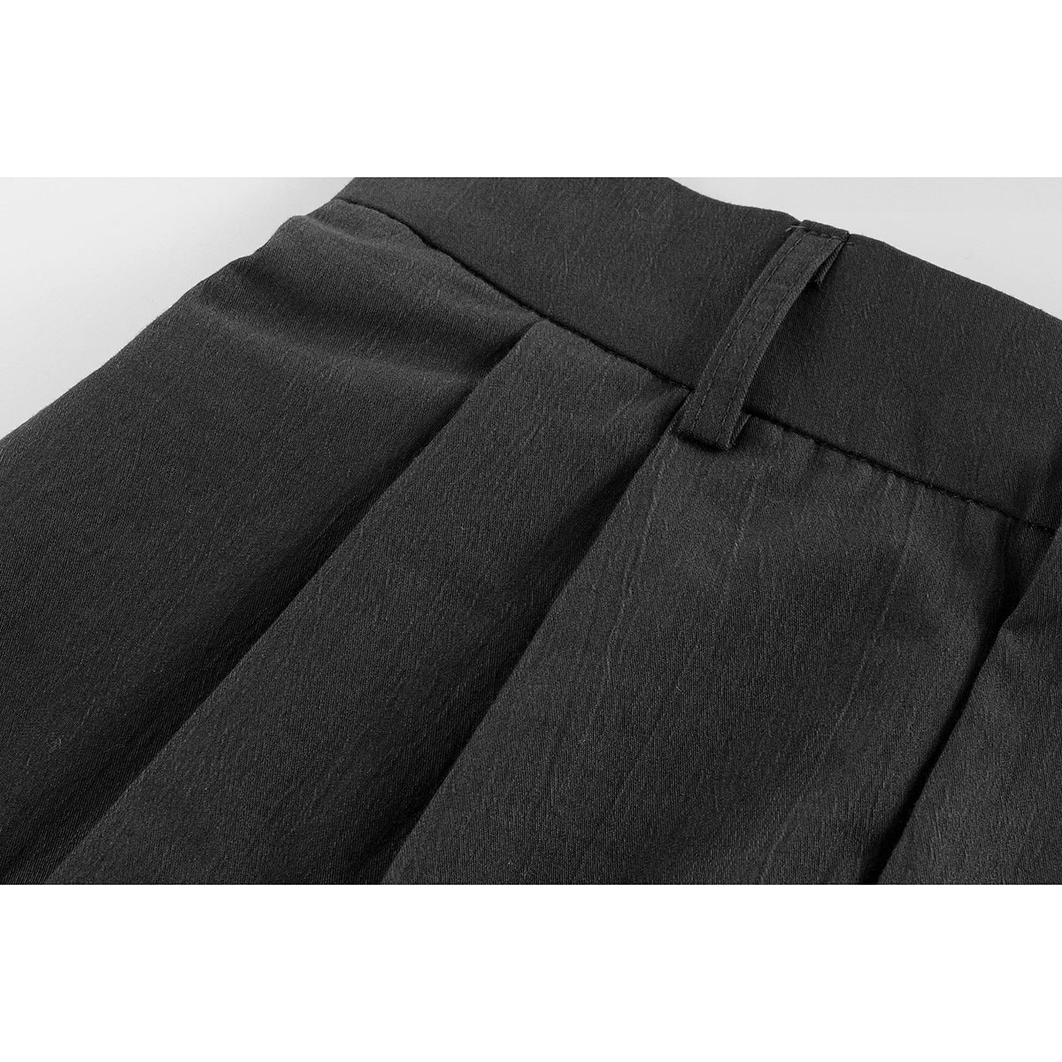 Close-up of black shorts showing a belt loop, waistband stitching and front pleats.