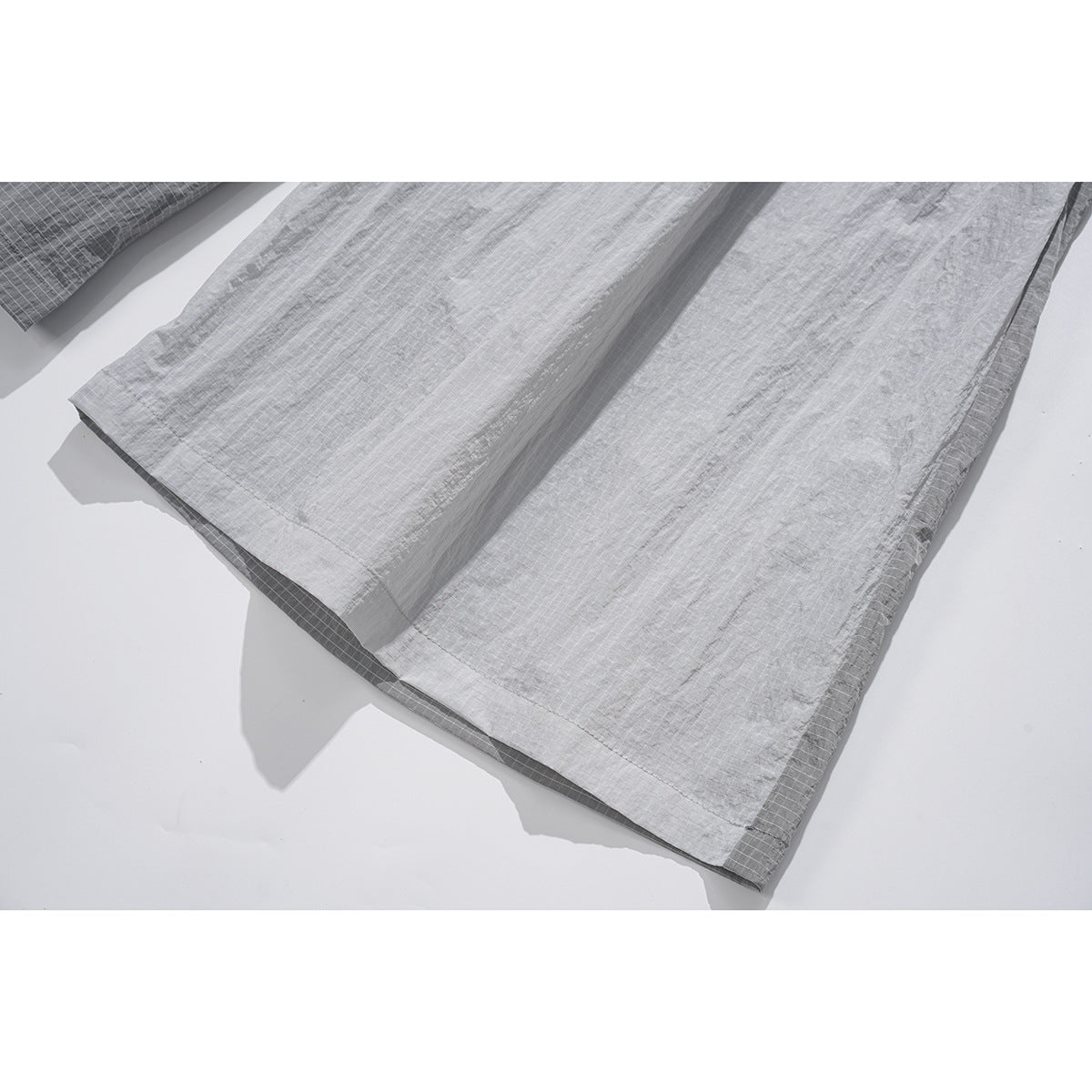 Close-up of the hem of light gray, grid-patterned wide-leg bottoms with a darker gray panel underneath.