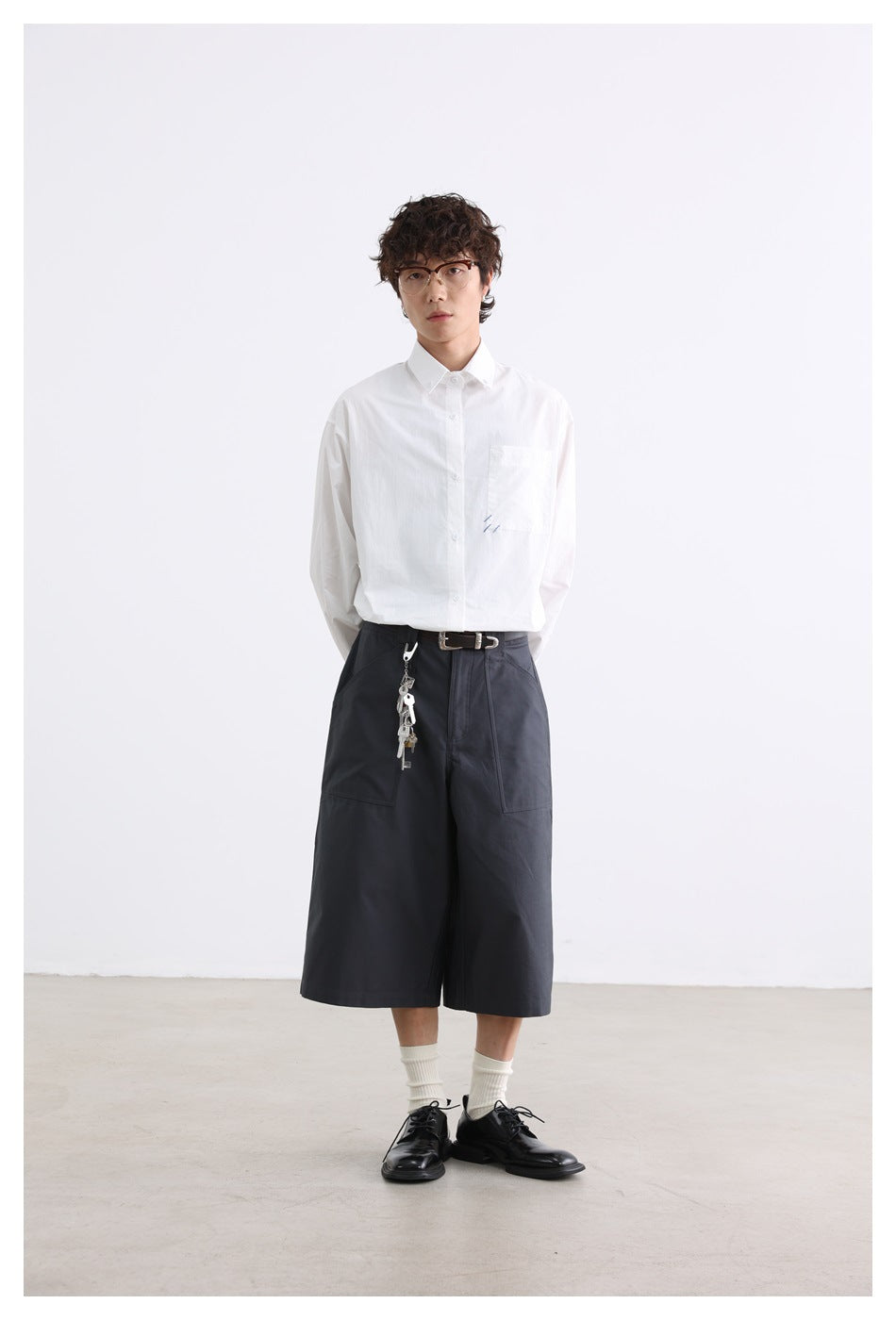 Model wearing a white long-sleeve button-up shirt with chest pocket and dark wide-leg shorts.