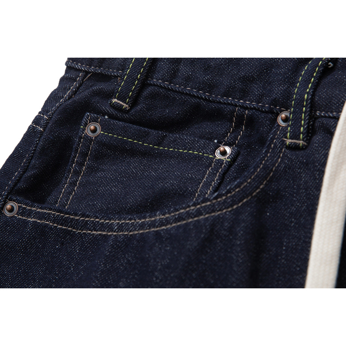 Close-up of a dark indigo jeans front pocket with metal rivets, contrast stitching, and a belt loop.