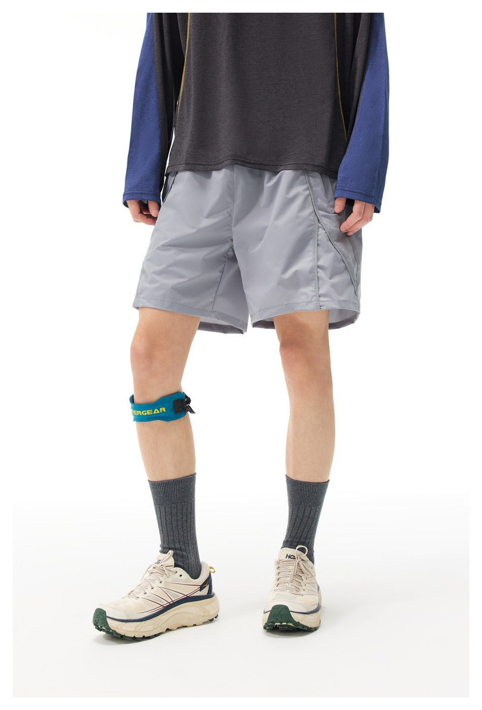Front view of a model wearing light gray athletic shorts with angled pockets and a dark color-block long-sleeve top.