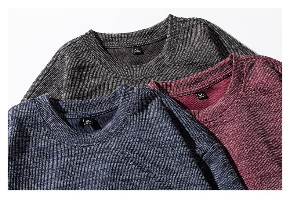 Three ribbed crewneck sweaters in charcoal, burgundy, and blue-gray overlap in a close-up.