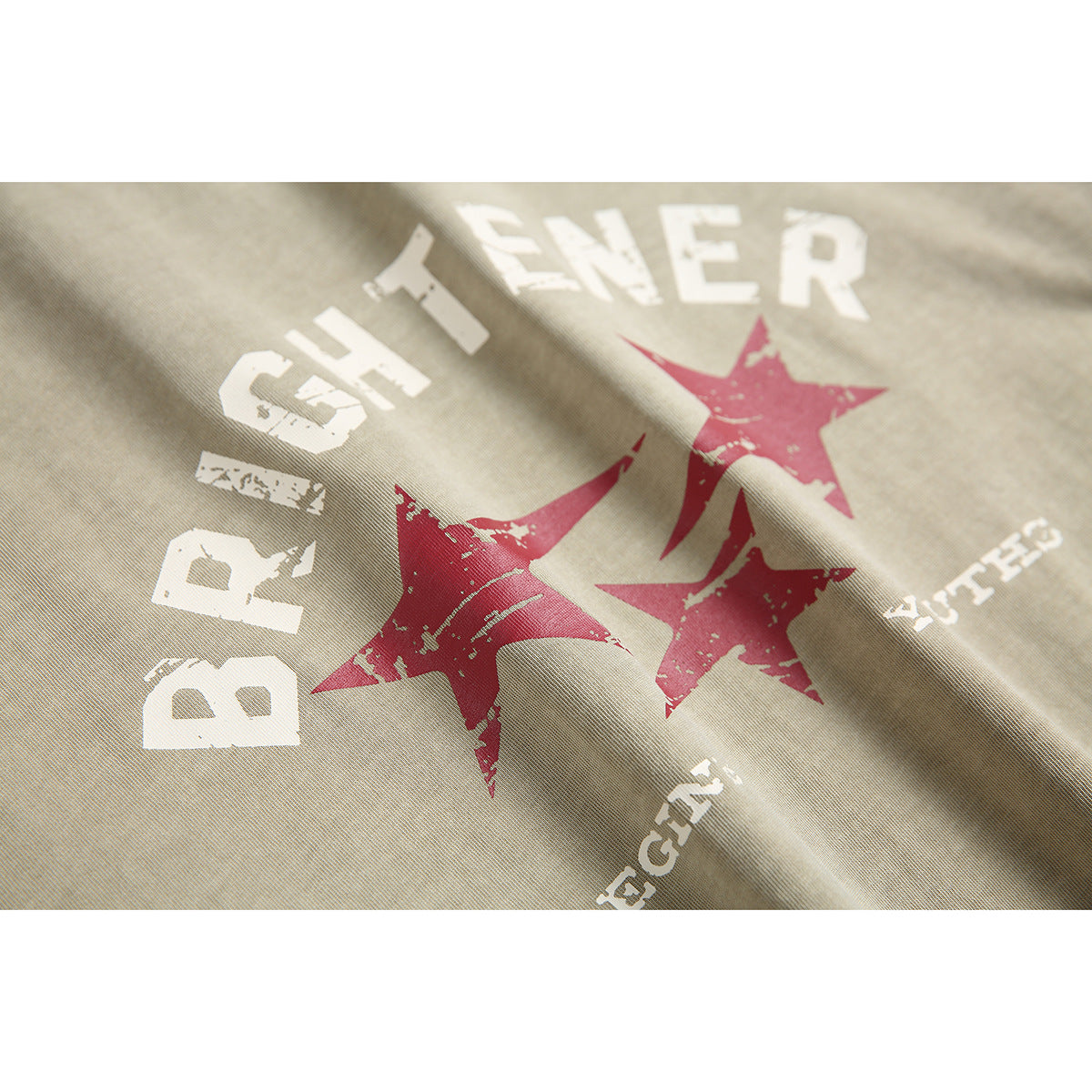Close-up of the distressed white lettering and red star graphic printed on beige T-shirt fabric.