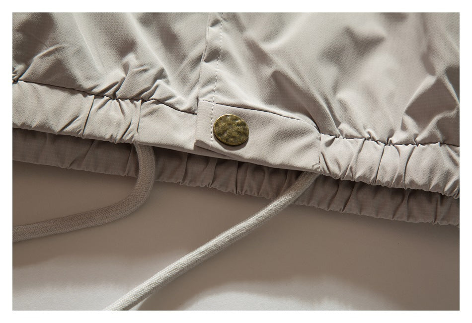Close-up of the jacket's gathered hem, brass-tone button, and hanging drawcords.