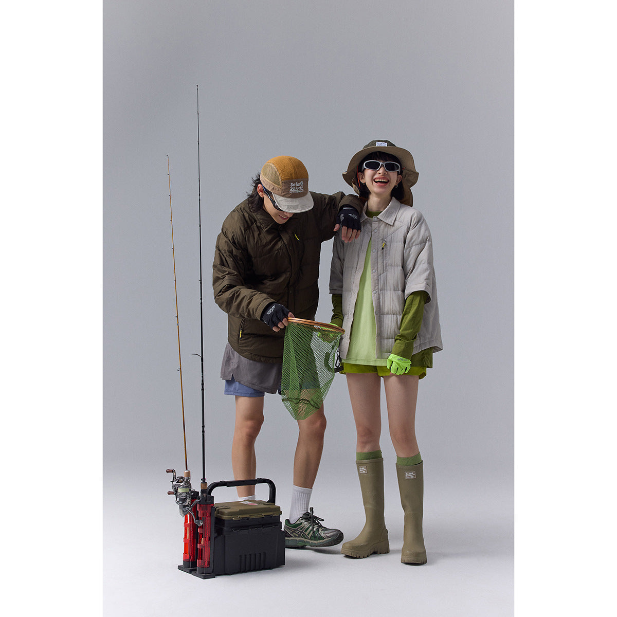 Two models wearing outdoor outfits, including dark brown and light gray quilted jackets, pose with fishing gear.