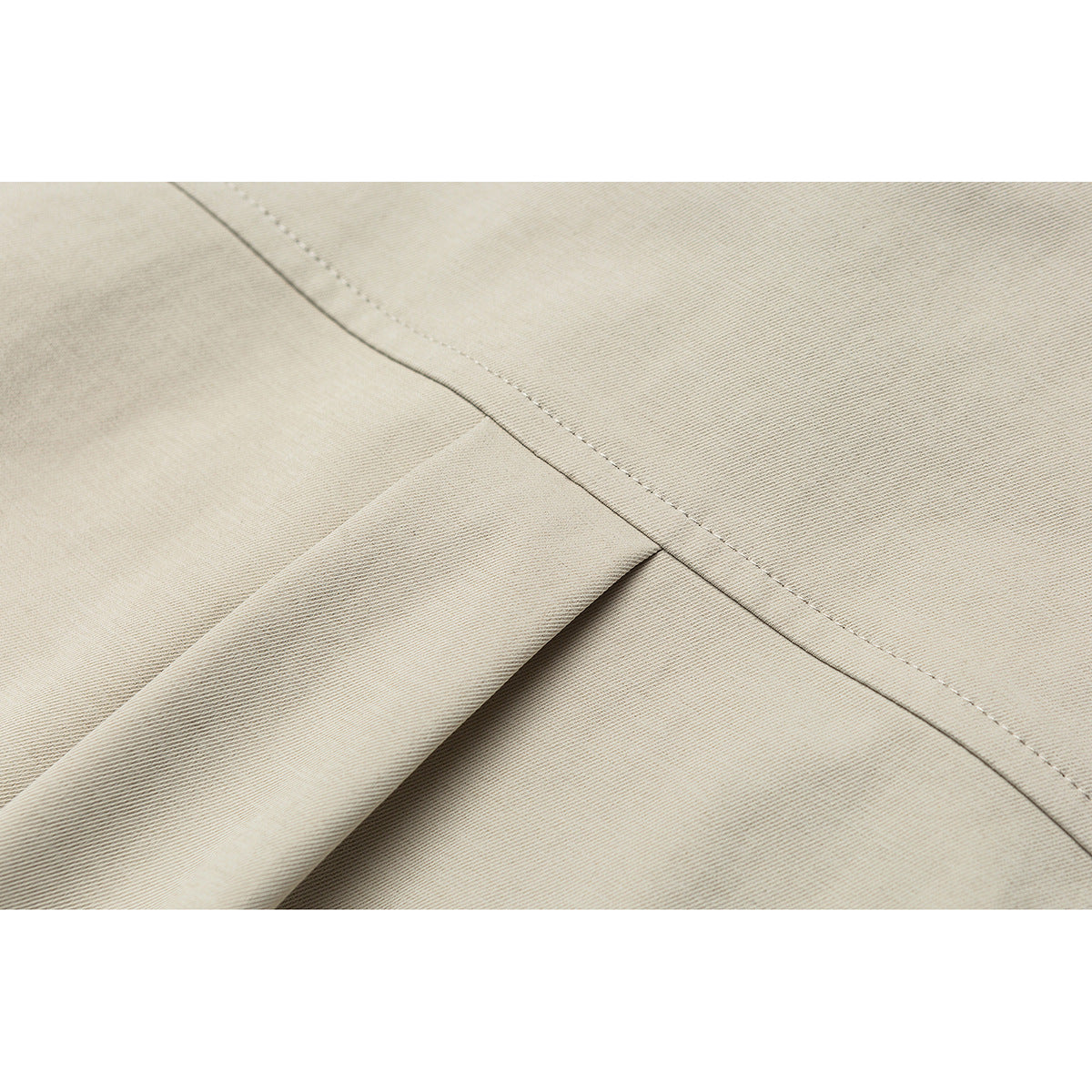 Close-up of beige garment fabric with a diagonal stitched seam and folded fabric edge.