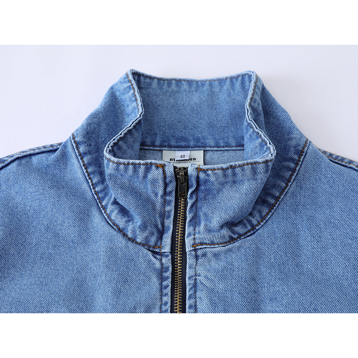 Close-up of a light blue denim jacket's high collar and front zipper, with a small neck label visible.