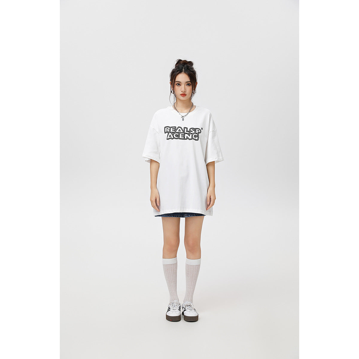 Full-length front view of a model in an oversized white T-shirt with black lettering and denim shorts.