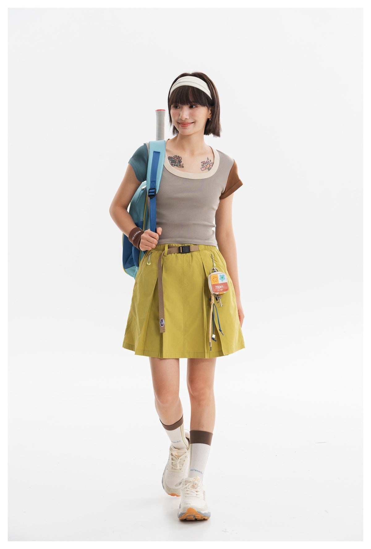 Model wearing a taupe color-block top and yellow-green skirt with a blue backpack.