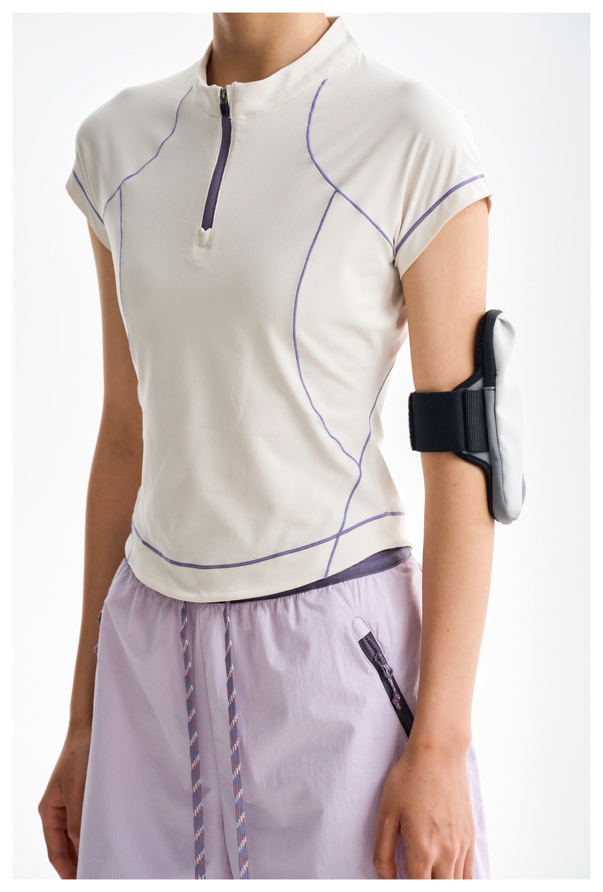 Close-up of a white zip-neck top with purple piping, paired with lavender shorts; a forearm phone holder is also visible.