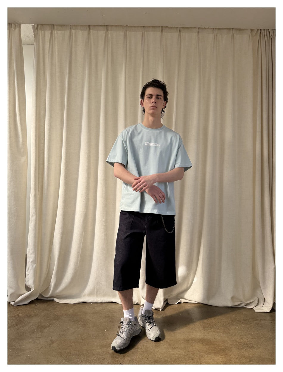 Full-length model wearing a pale blue short-sleeve T-shirt with a small chest print and black shorts.