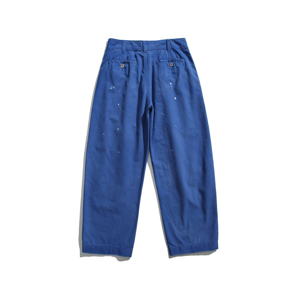 Full-length front view of cobalt-blue wide-leg trousers with belt loops, buttoned pockets and white paint-like speckles.