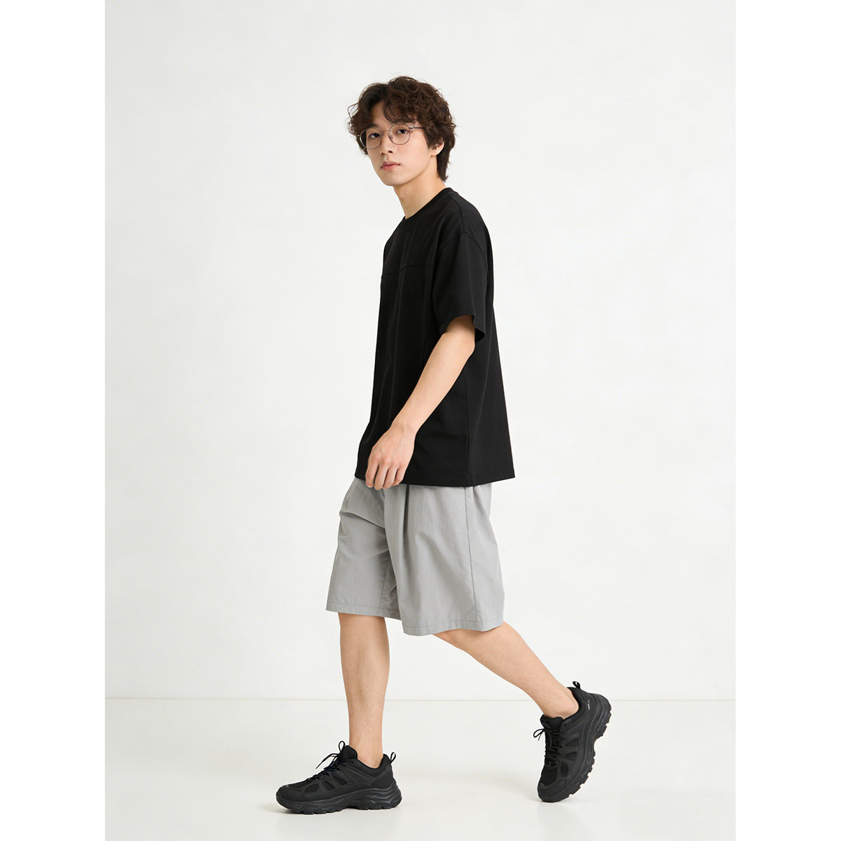 Model walking in a black oversized short-sleeve crewneck T-shirt with a horizontal chest seam.