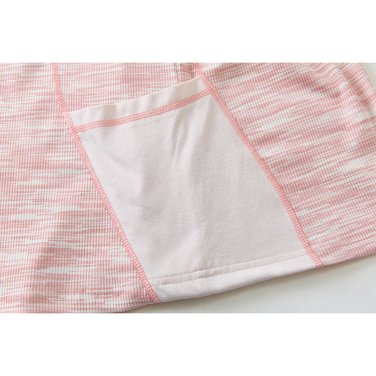 Close-up of a pale pink rectangular pocket with pink stitching on a pink-and-white patterned top.