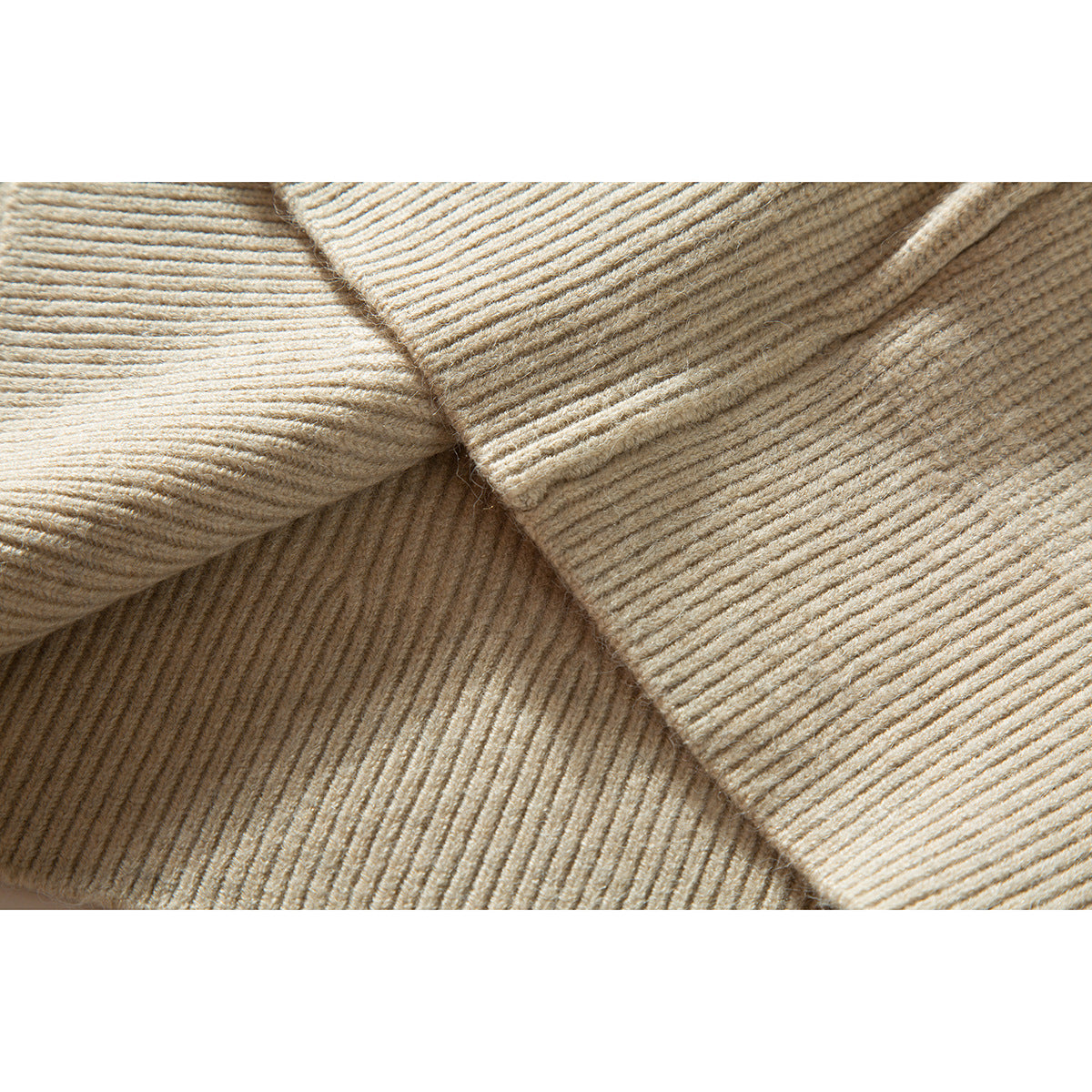 Close-up showing the ribbed knit texture and overlapping folds of a cream sweater.