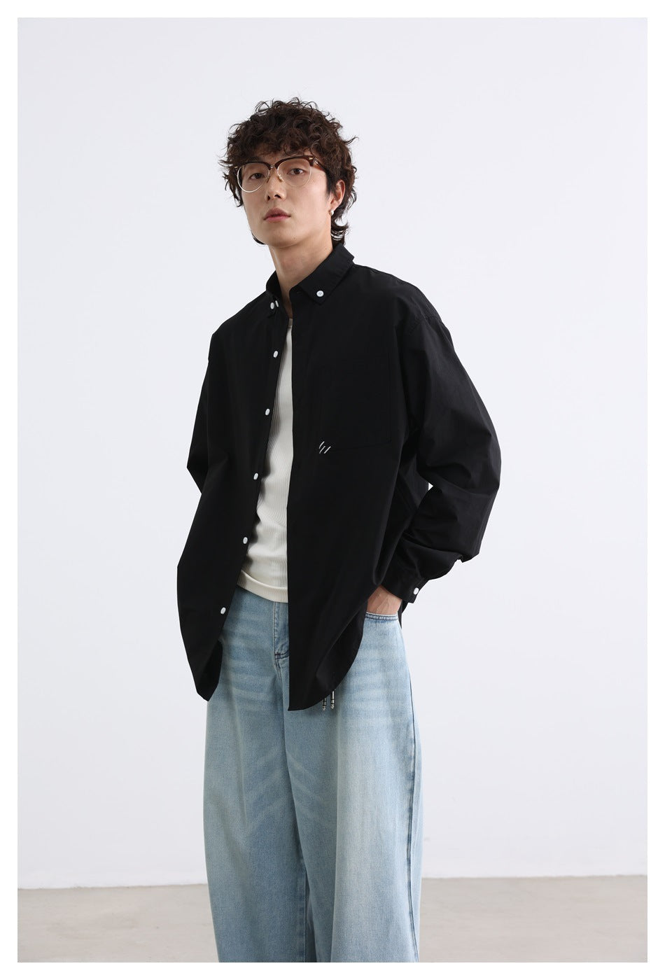 Model wearing a black button-up shirt with a chest pocket over a white top and light blue jeans.