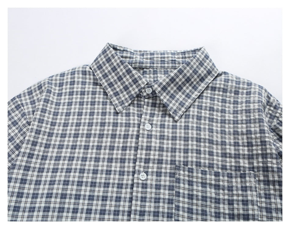 Close-up of the blue-gray plaid shirt front, showing its pointed collar, white buttons, and chest pocket.