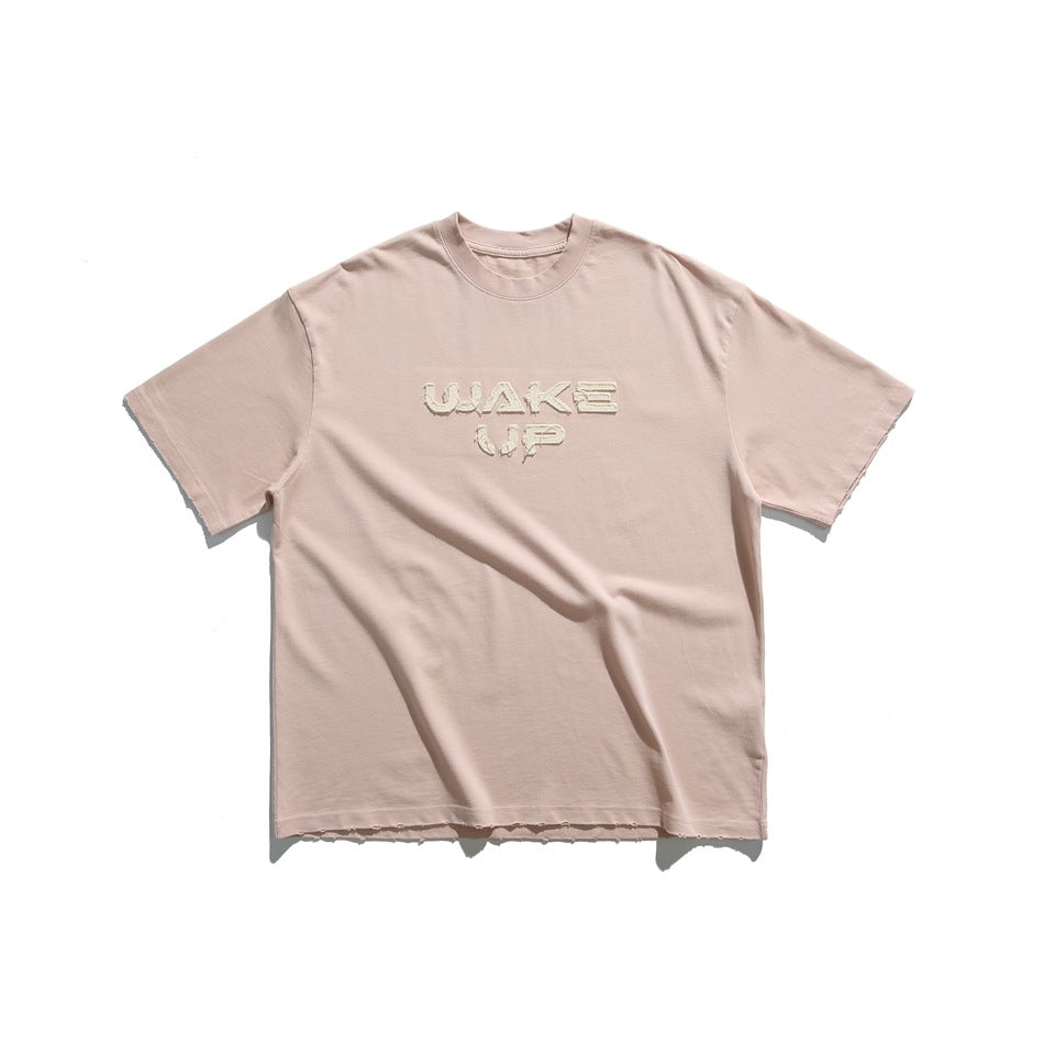 Pink short-sleeve crew-neck T-shirt with frayed beige WAKE UP appliqué lettering, flat lay