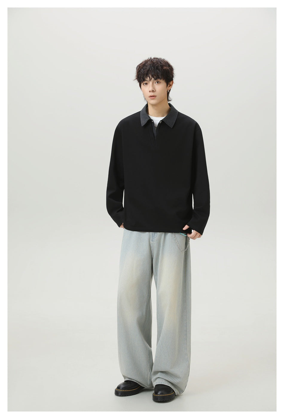 Model wearing a black long-sleeve top with a charcoal collar and V-placket, styled with pale striped wide-leg pants.