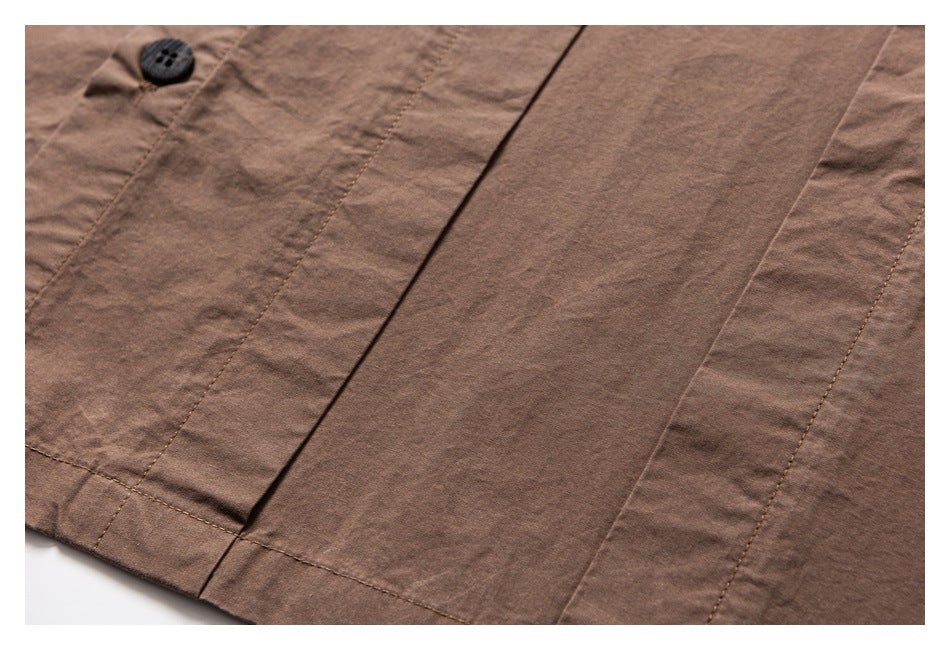 Close-up of a dark button and stitched vertical panels on a brown garment.