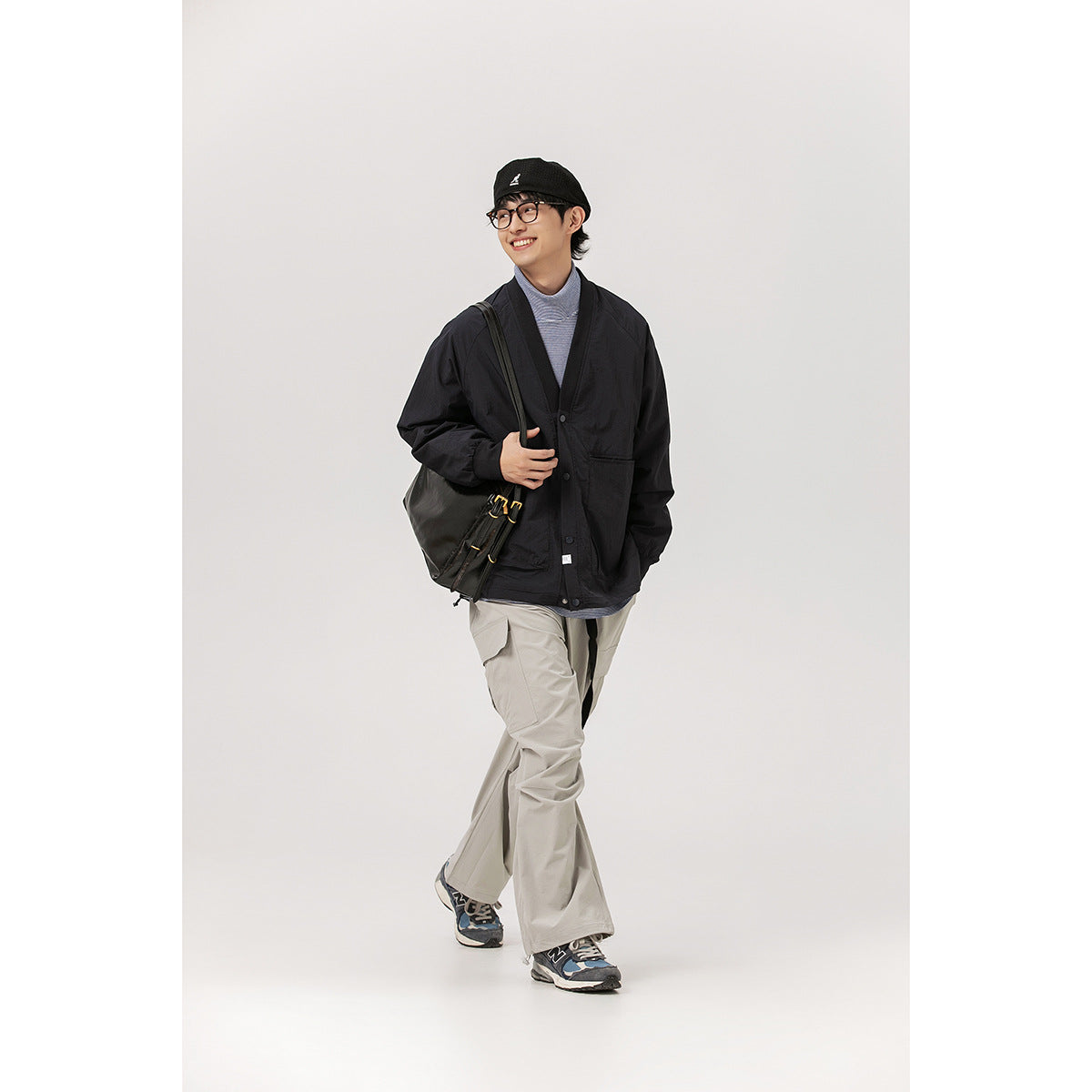 Full-length model wearing a black cardigan jacket, striped top, light gray pants, and a black shoulder bag.