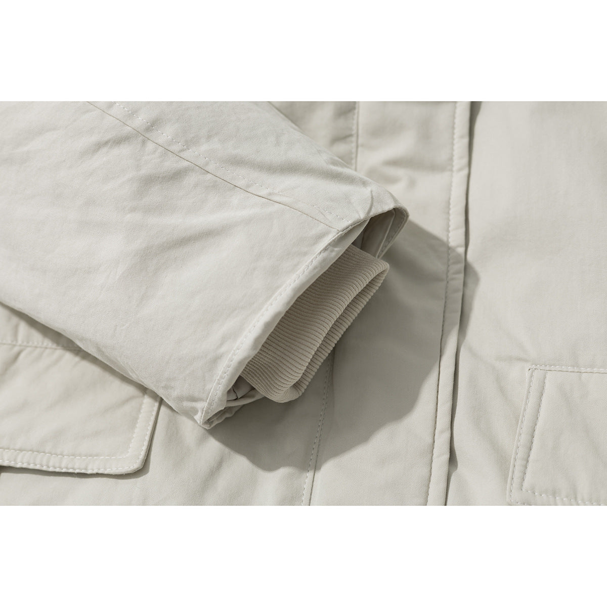 Close-up of an ivory coat sleeve showing a ribbed inner cuff, stitching, and part of a pocket.