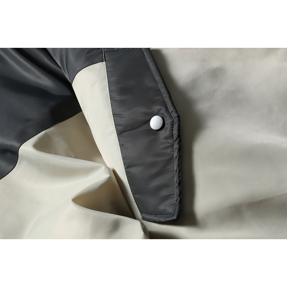 Close-up of a light gray jacket pocket flap with a round snap fastener and black trim.