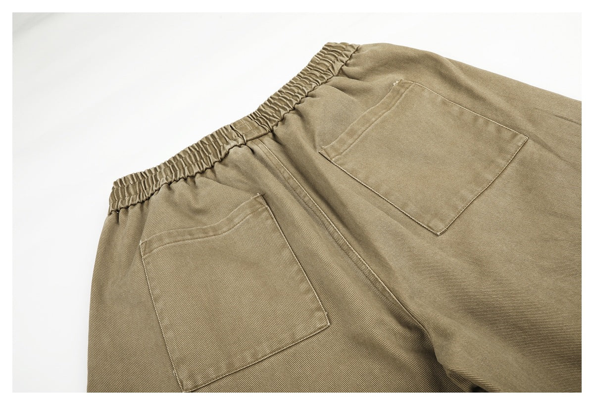 Cropped view of tan trousers from the back, showing the elastic waist and two patch pockets.