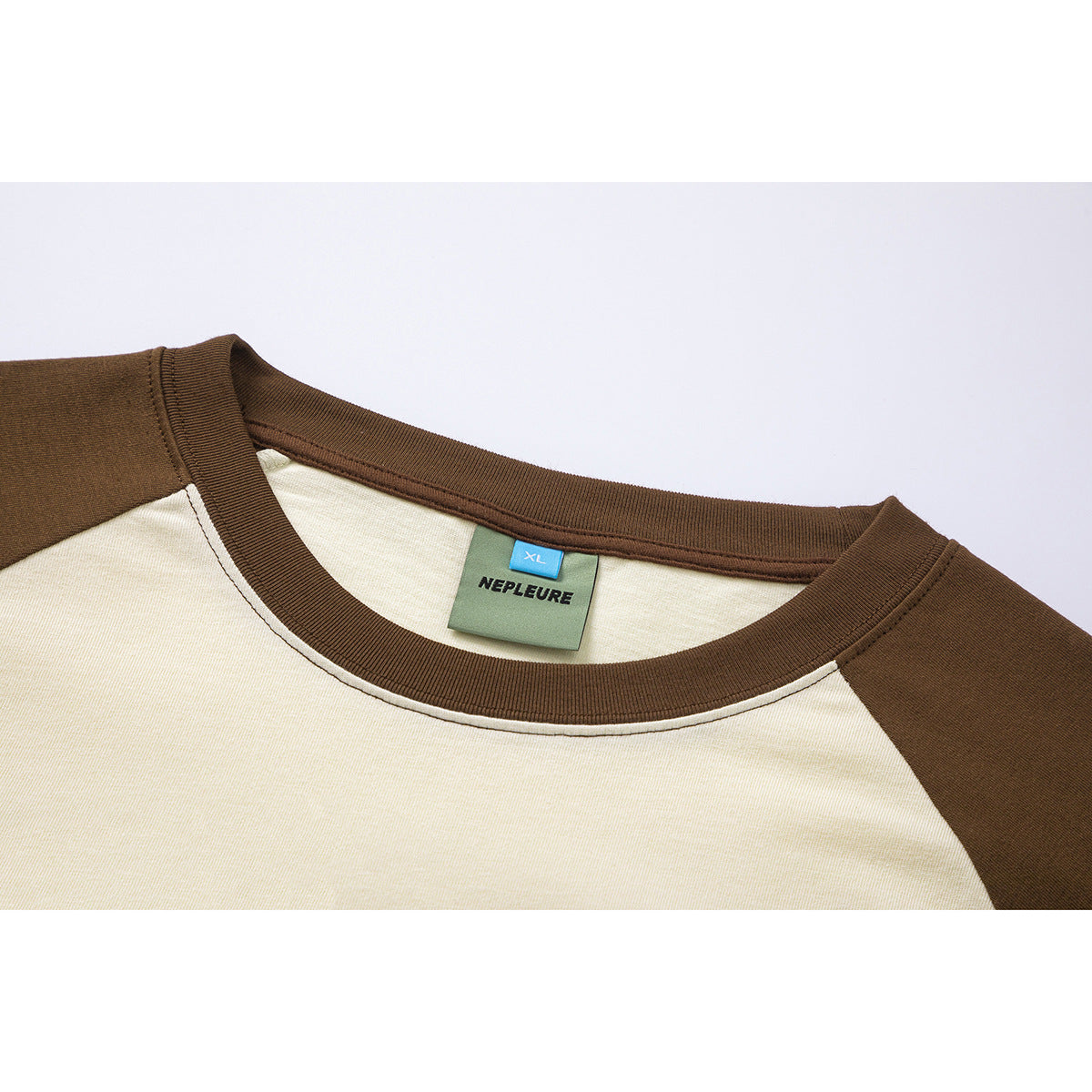 Close-up of a cream raglan T-shirt with a brown ribbed crew neck and a visible XL brand label.