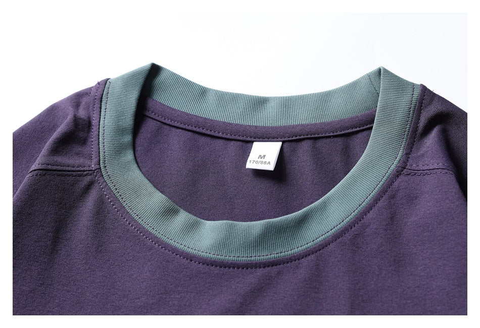 Close-up of the purple sweatshirt's muted teal ribbed crew neckline and small size tag.