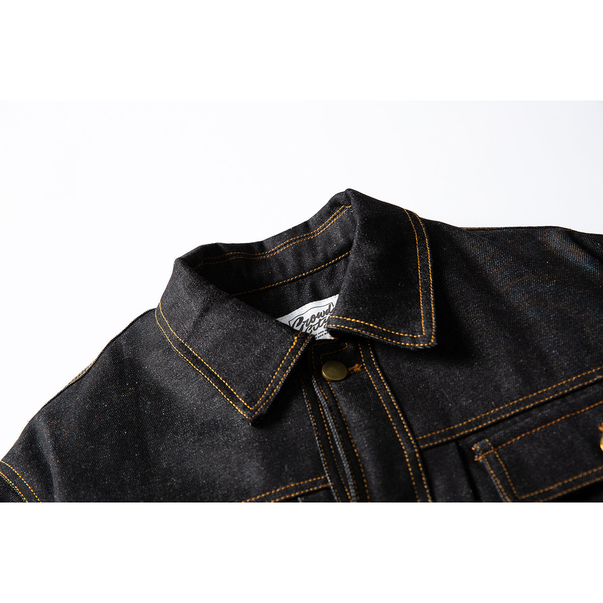 Close-up of a dark denim jacket collar and upper chest with contrast golden stitching and a brass-tone button.