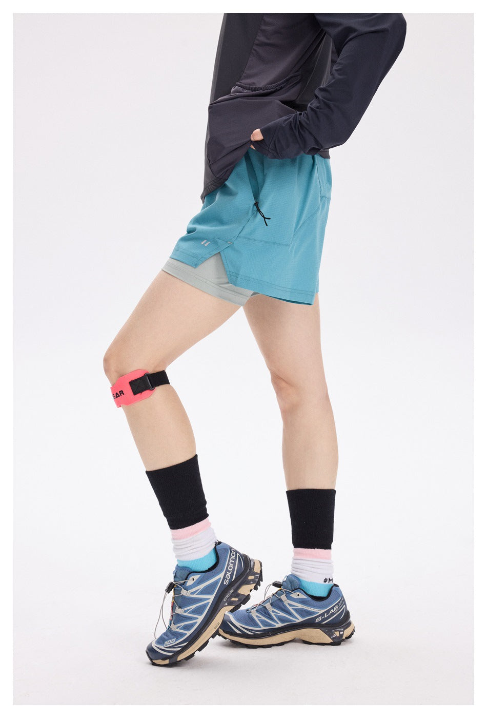 Side view of a model wearing turquoise running shorts over gray liner shorts.