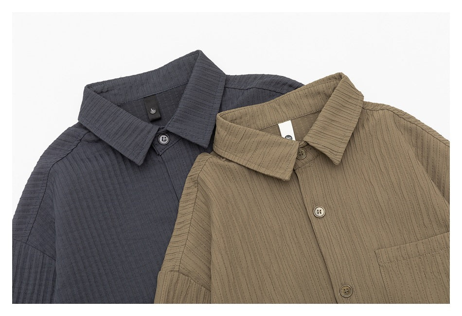 Close view of charcoal and taupe button-up shirts, showing their collars, buttons, chest pockets, and textured stripes.