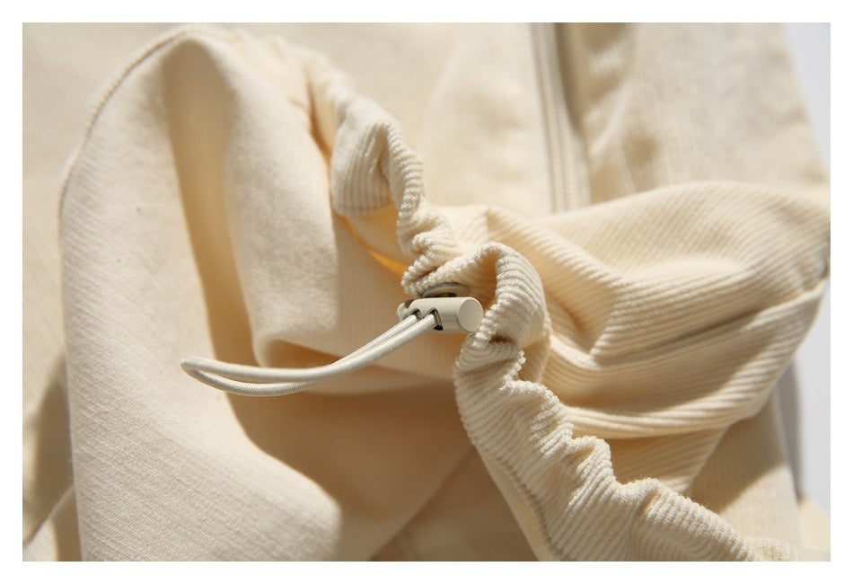 Close-up of the cream garment's gathered hem drawcord and cord lock.