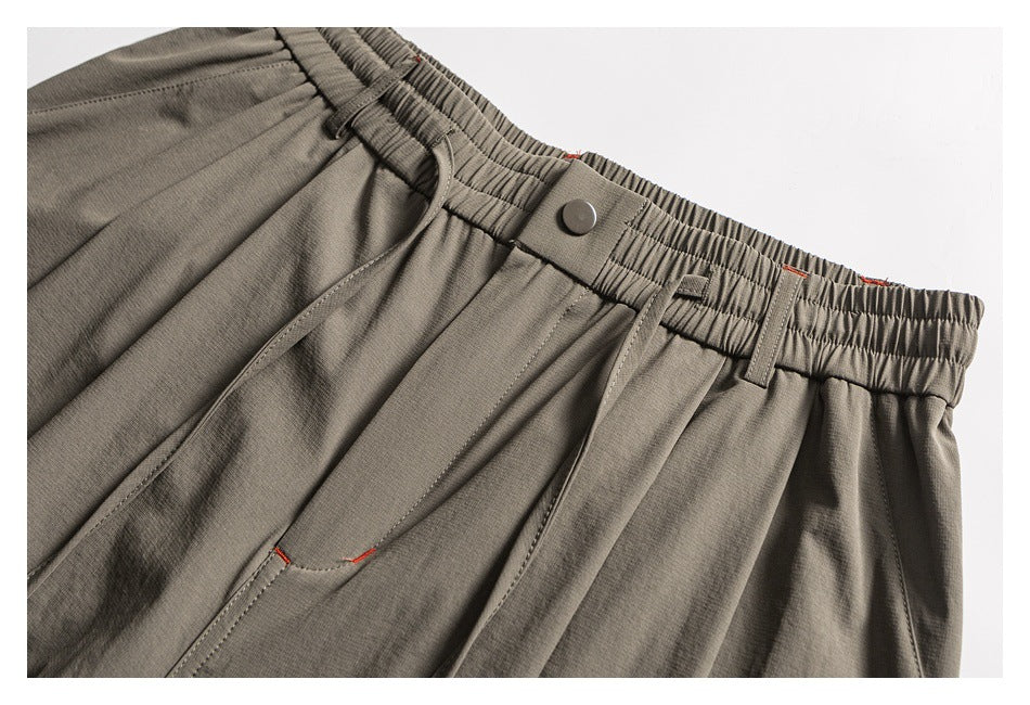 Close view of taupe trousers showing the elastic waistband, button, belt loops, and front pockets.