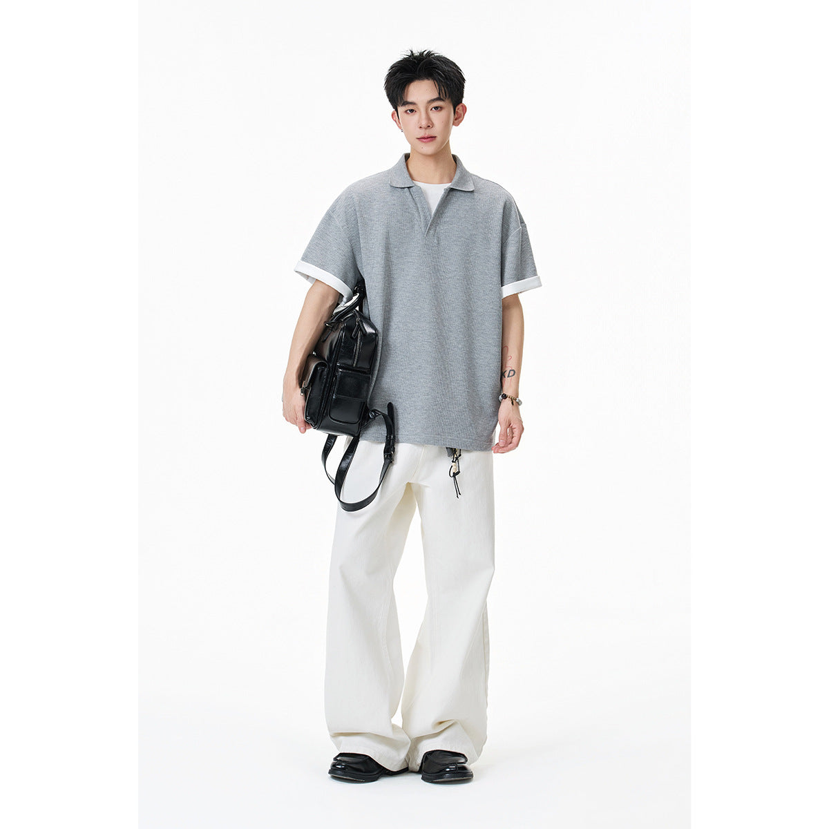 Model wearing a gray short-sleeve polo with white sleeve cuffs and loose white trousers.