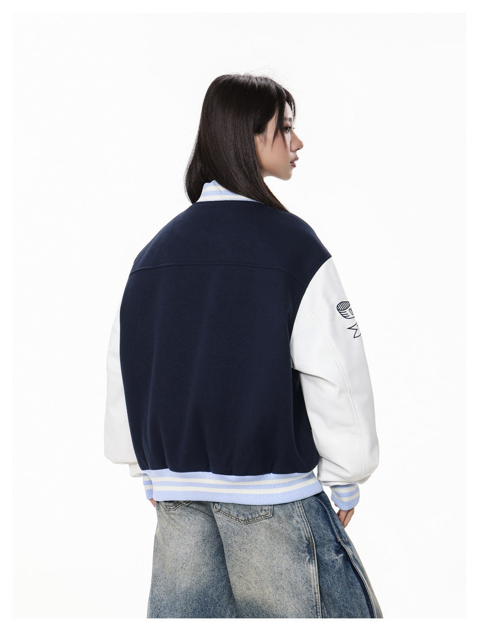 Model showing the back of a navy varsity jacket with white sleeves and blue-and-cream striped ribbed trim.